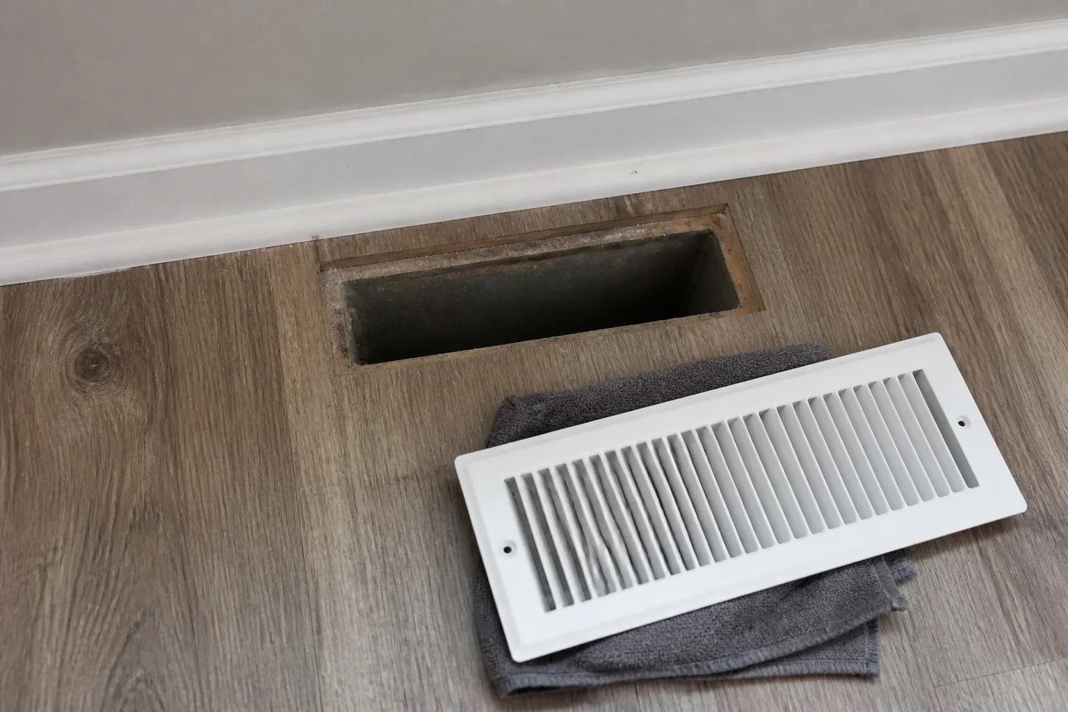 White floor register on a folded cloth beside an open floor vent.